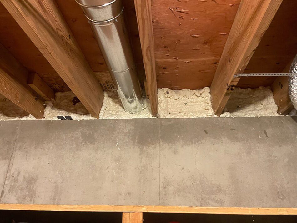 Spray foam insulation applied to basement rim joists to seal air leaks and prevent drafts near floor joists and HVAC ductwork.