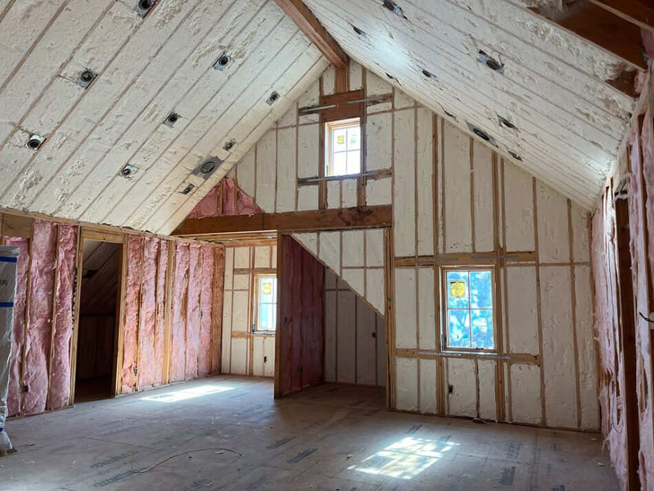 Vaulted ceiling with spray foam insulation and pink fiberglass batts in a residential room to maximize thermal efficiency.