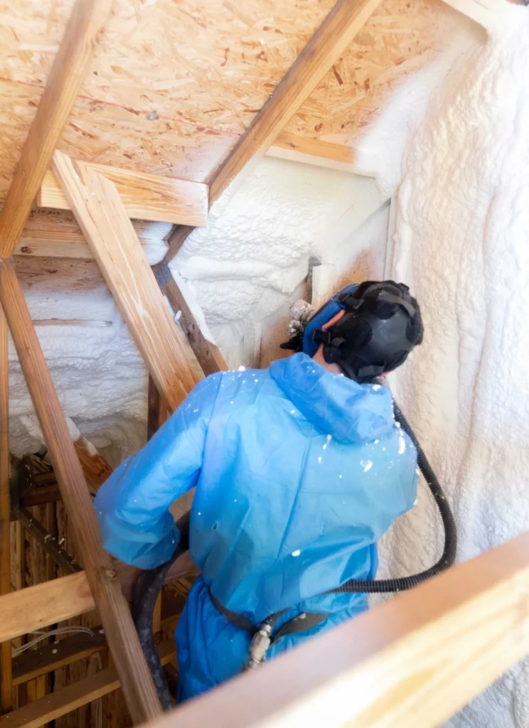 Professional installer applying spray foam insulation to an attic roof deck to improve home climate control.