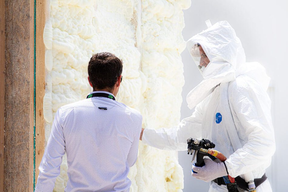 Professional spray foam contractor in a white safety suit discussing the installation process with a homeowner next to freshly applied foam.