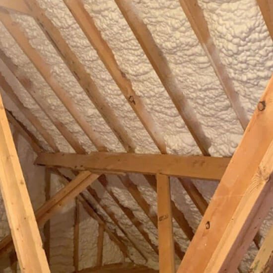 Attic roof deck insulated with spray foam between wooden rafters to create a conditioned space and improve energy efficiency.